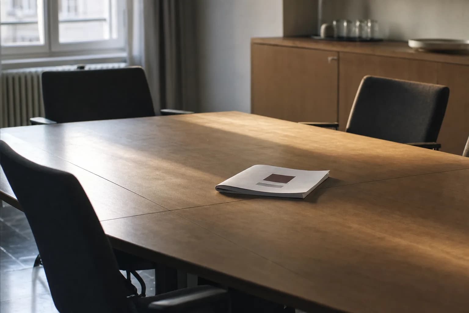Un rapport imprimé posé fermé sur une table de réunion vide après une réunion, chaises de travers, lumière de fin d'après-midi